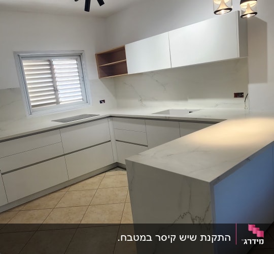 משטחי שיש לבנים במטבח מודרני עם תאורה תלויה.